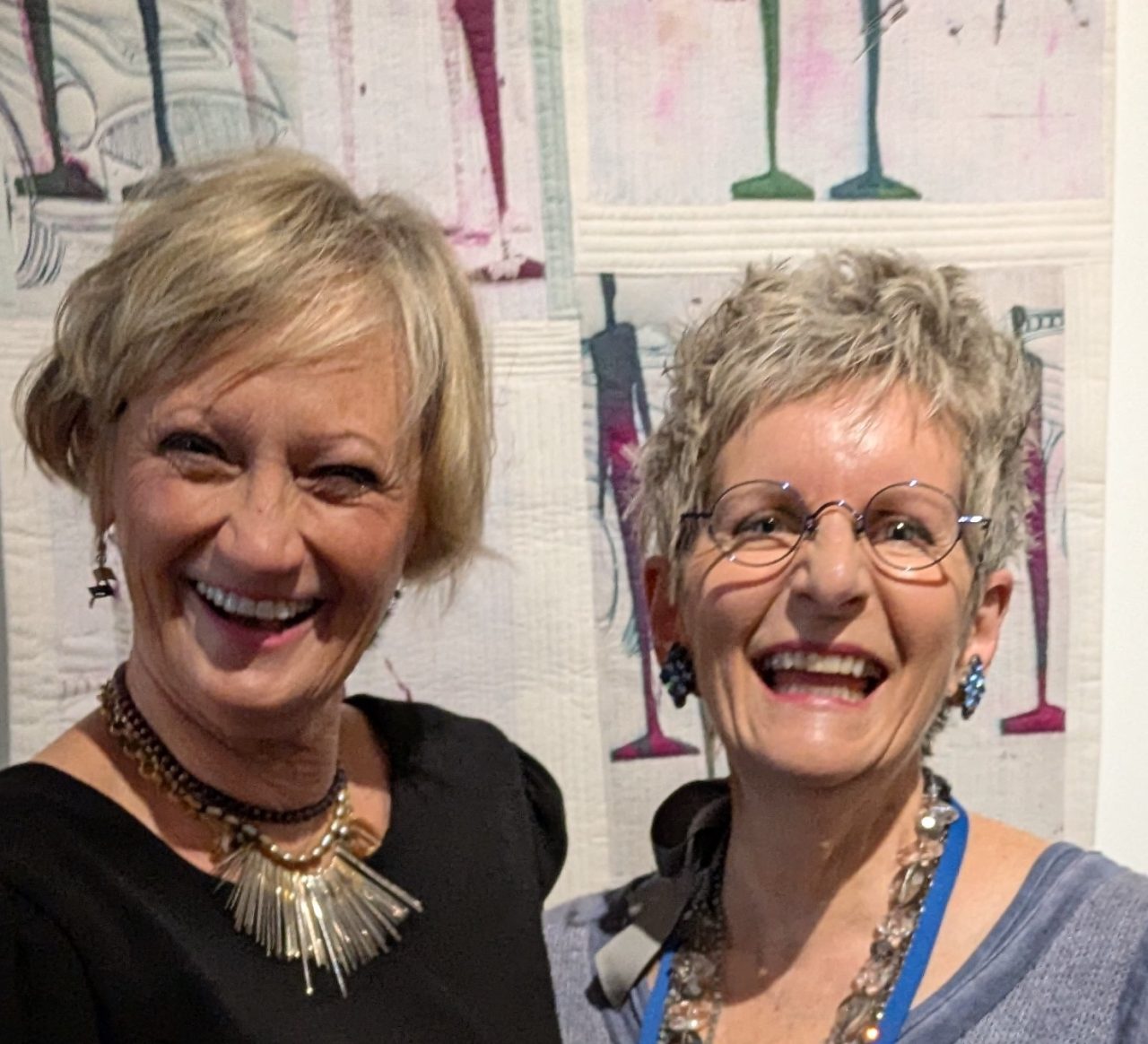 Two smiling women with a quilt backdrop