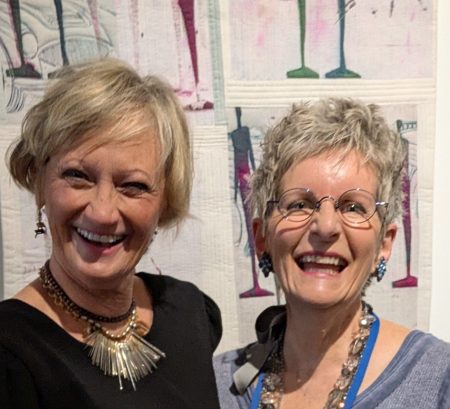 Two smiling women with a quilt backdrop